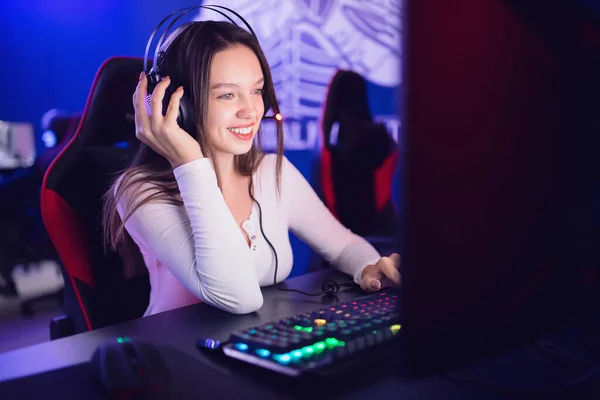 A smiling streamer in headphones at a keyboard in a neon-lit booth with a gaming chair behind her